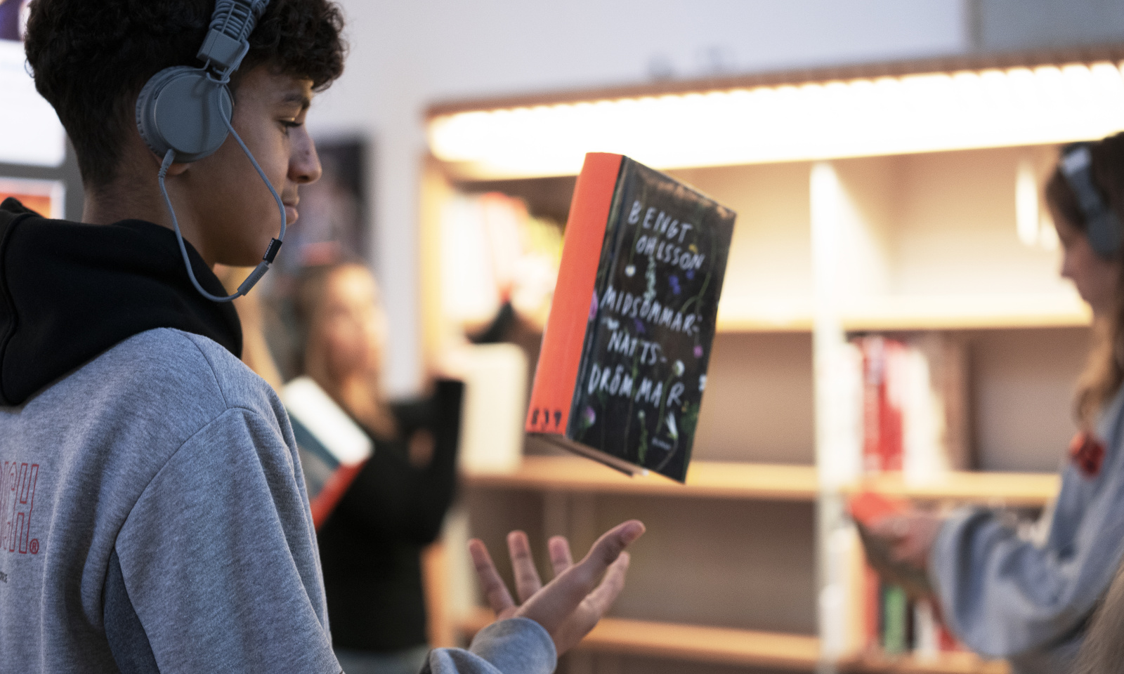 Pojke med hörlurar i ett bibliotek kastar upp en bok i luften.