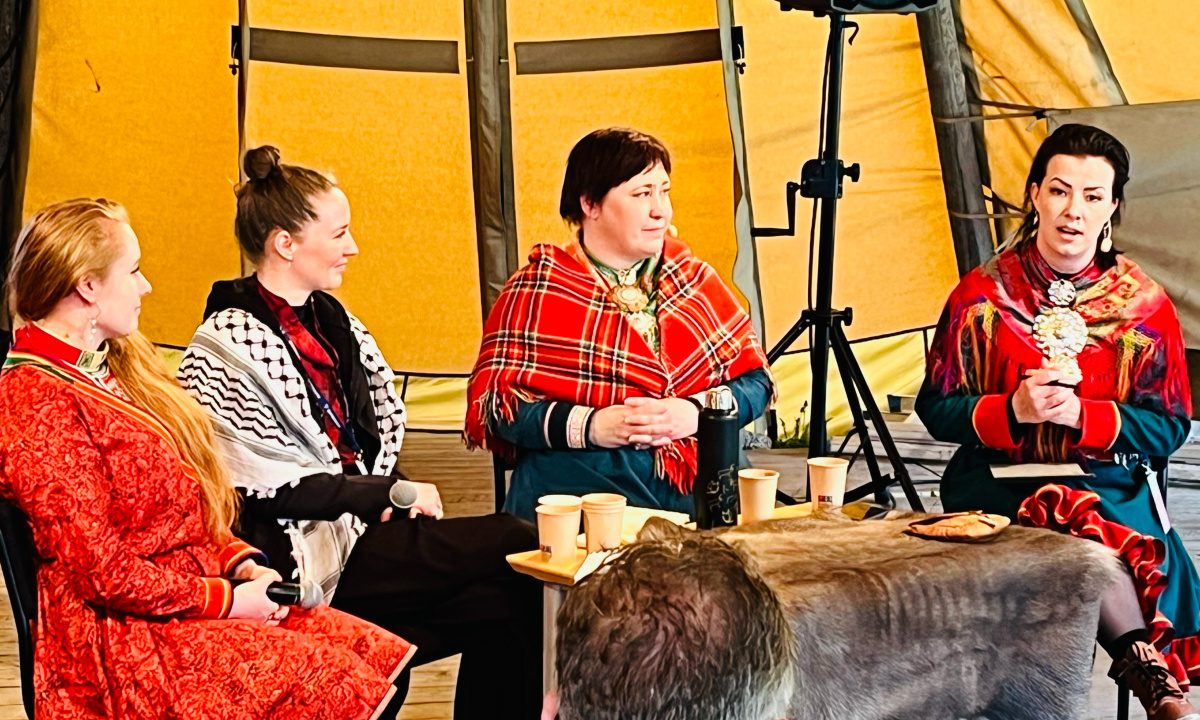 Fyra kvinnor i traditionella samiska kläder sitter och samtalar i en kåta.