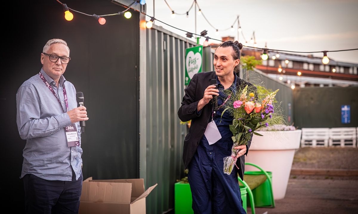 Två män på scen varav en håller i en blombukett