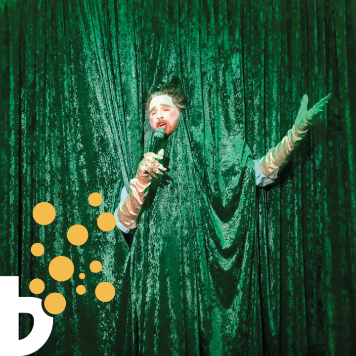 En sjungande person insvept i grönt glitterdraperi